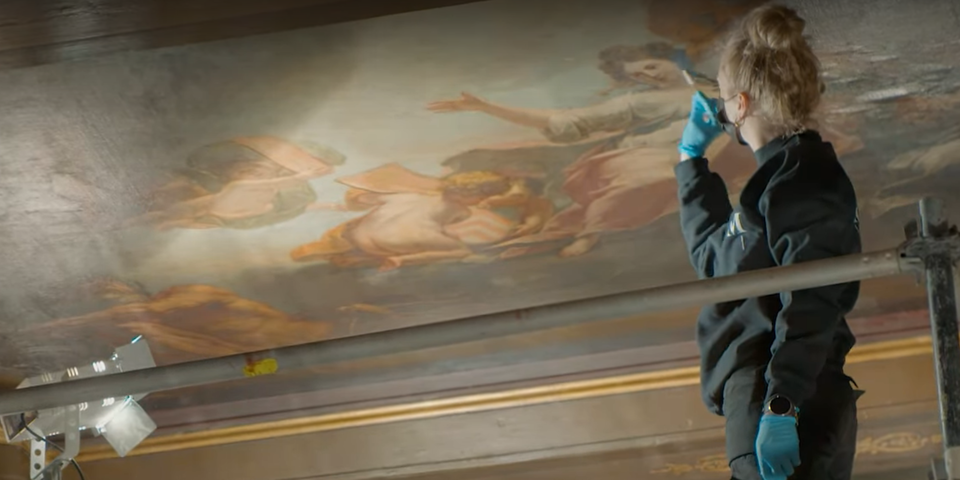 Een restaurator herstelt een plafondschildering op het Schoon Verdiep.